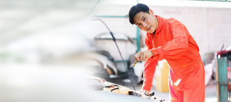 Senior Asian man checking or measuring a vehicle oil engine or engine lubricant level by using oil stick indicator. Senior professional repairman inspecting an oil engine in an old car.の写真素材