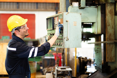 Professional caucasian white ethnicity male technician operating the heavy duty machine in the lathing factory. Technician in safety and helmet suit controlling a machine in factory.の写真素材