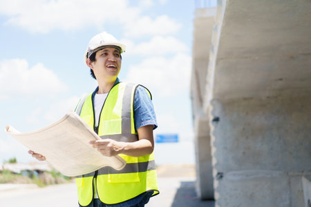 Asian professional - senior cilvil or construction engineer inspecting a segmenting bridge blueprint and construction plan at the site, civil engineer working at bridge construction site.の写真素材