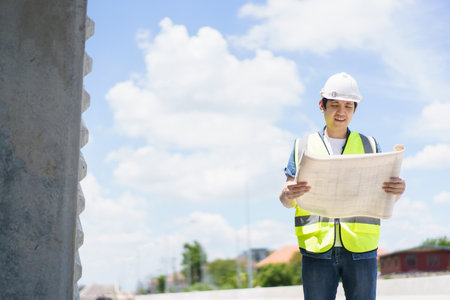 Asian professional - senior cilvil or construction engineer inspecting a segmenting bridge blueprint and construction plan at the site, civil engineer working at bridge construction site.の写真素材