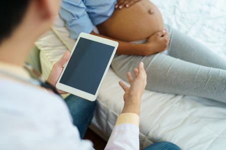 Asian male doctor visit to African - American pregnant woman patient home to talk and check for pregnancy health. On site - home medical service concept.の写真素材