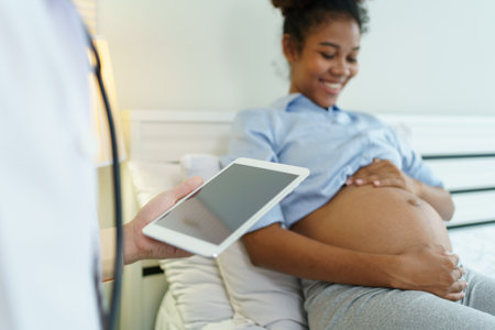 Asian male doctor visit to African - American pregnant woman patient home to talk and check for...