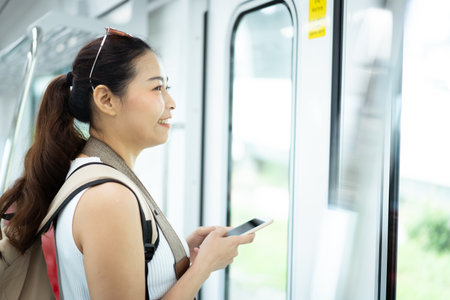 Beautiful Asian woman tourist - passenger looking for the city map on her smartphone while traveling on a train. Woman passenger using mobile phone searching for a transportation information.の写真素材