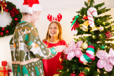 Happy young brother and sister enjoy decorating their Christmas tree together with a fantasy - festive balls and presents, a boy helping his older sister decorates Christmas tree.の写真素材