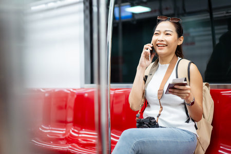 Beautiful Asian woman tourist - passenger looking for the city map on her smartphone while traveling on a train. Woman passenger using mobile phone searching for a transportation information.の写真素材