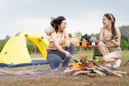 Happy Asian women light a fire near their camping site together prepare for cooking and warmth. Women enjoy camping activity.の写真素材