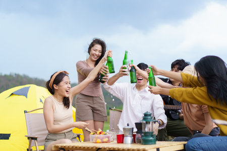 Group of Asian young adult people enjoy drinking a beer together during camping at the park. Asian young women and men celebrating with a bottle of a beer together.の写真素材