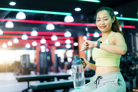 Asian good looking sportswoman taking a rest after finished workout and looking at smartwatch for exercise tracking. Sportswoman using fitness tracker or smartwatch.の写真素材
