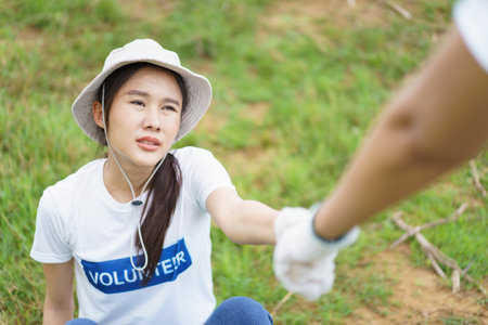 Friends helps and supports each other while doing the voluntary activity, woman pulling her tired friend from the ground.の写真素材