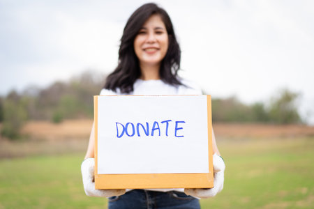 Happy Asian beautiful woman working as a volunteer holding a donation cardboard box portrait. Voluntary and charity works for humanity and sustainable concept. Female volunteer smiles to camera.の写真素材
