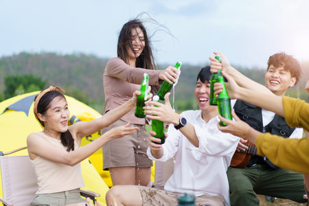 Group of Asian young adult people enjoy drinking a beer together during camping at the park. Asian young women and men celebrating with a bottle of a beer together.の写真素材