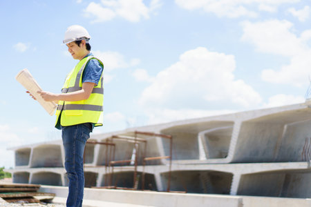 Asian professional - senior cilvil or construction engineer inspecting a segmenting bridge blueprint and construction plan at the site, civil engineer working at bridge construction site.の写真素材