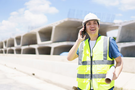 Asian professional - senior cilvil or construction engineer inspecting a segmenting bridge blueprint and construction plan at the site, civil engineer working at bridge construction site.の写真素材