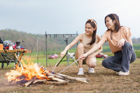 Happy Asian women light a fire near their camping site together prepare for cooking and warmth. Women enjoy camping activity.の写真素材