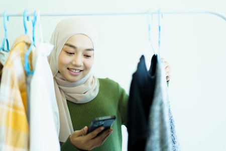 Happy cheerful Asian young muslim woman choosing a clothes in fitting room on a clothing hanger. Modern lifestyles concept of muslim people.の写真素材