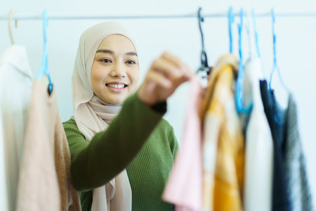 Happy cheerful Asian young muslim woman choosing a clothes in fitting room on a clothing hanger. Modern lifestyles concept of muslim people.の写真素材