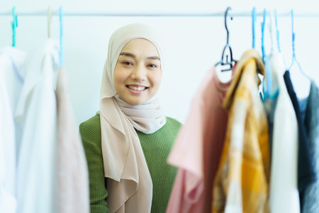 Happy cheerful Asian young muslim woman choosing a clothes in fitting room on a clothing hanger. Modern lifestyles concept of muslim people.の写真素材