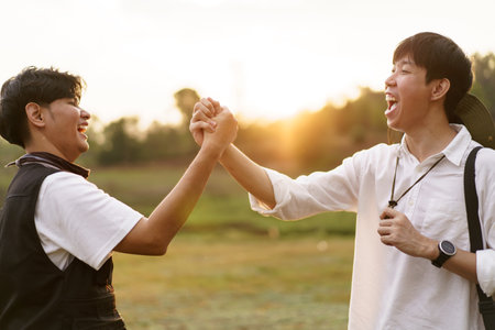 Happy Asian men looking at the beautiful sunlight during the sunset behind mountain together. Friends touch - hold hands together.の写真素材
