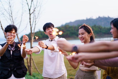 Group of Asian young men and women celebrating together with a sparkling firework in the evening. Happy men and women enjoy playing a sparklers firework in a party.の写真素材
