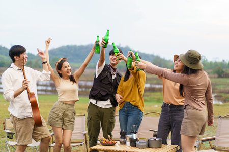 Group of Asian young adult people enjoy drinking a beer together during camping at the park. Asian young women and men celebrating with a bottle of a beer together.の写真素材
