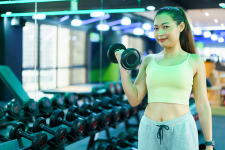 Active Asian sportswoman doing a weight training workout in indoor gym, Asian beautiful woman lifting a dumbbell.の写真素材