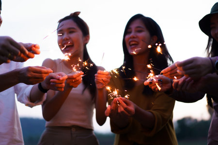 Group of Asian young men and women celebrating together with a sparkling firework in the evening....