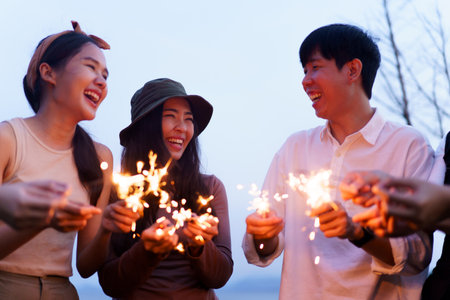 Group of Asian young men and women celebrating together with a sparkling firework in the evening....