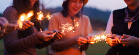 Group of Asian young men and women celebrating together with a sparkling firework in the evening. Happy men and women enjoy playing a sparklers firework in a party.の写真素材