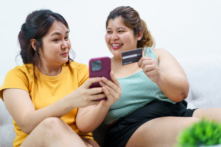 Happy Asian fat women friend excited in online shopping with special discount and using credit card to make a payment. Two Asian fat women staying together and buying goods in e-commerce website.の写真素材