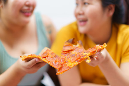 Happy oversize fat Asian women enjoy eating a pizza, hamburger, and French fry with drinking cola soda together. Unhealthy eating and unhealthy lifestyles concept.の写真素材