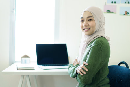 Happy Asian beautiful muslim woman wearing hijab working in front of the laptop - notebook computer at home, modern muslim working lifestyles concept. Muslim young woman working at home.の写真素材