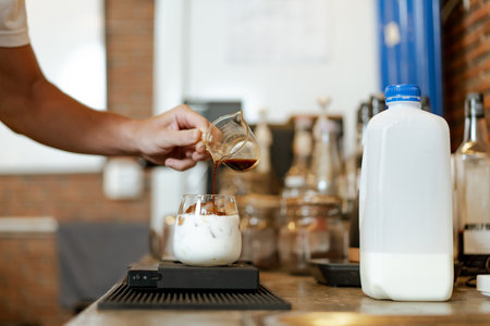 Professional Asian male barista pouring a cold milk in a glass. Happy male barista making a cup of iced latte coffee in a small coffee shop. Small business concept.の写真素材