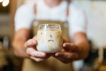 Professional Asian male barista pouring a cold milk in a glass. Happy male barista making a cup of iced latte coffee in a small coffee shop. Small business concept.の写真素材