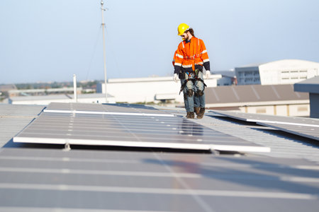 Professional electric engineers survey and inspect solar panels installation on the factory metal sheet roof top, electric engineer team inspecting and check solar cell system.の写真素材