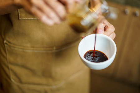 Professional Asian female barista pouring a shot of espresso into a coffee cup close up. Happy female barista making a cup of espresso coffee in a small coffee shop. Small business concept.の写真素材