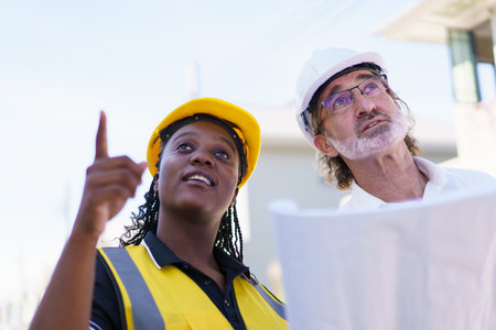 Team of engineer discuss at construction site. Female black ethnicity engineer taking to caucasian white client about the construction plan in blue print.の写真素材