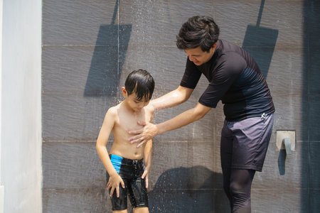 Father let his son taking a shower to clean his body before going to the swimming pool.の写真素材