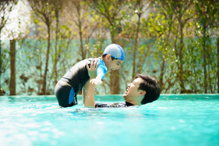 Happy cheerful Asian father and son playing and swimming together in the swimming pool, a boy enjoy playing a water with his dad. Summer and vacation activities in family.の写真素材