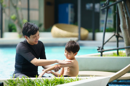 Father is applying a sun screen or sun block lotion on his son body before going to swimming in the...