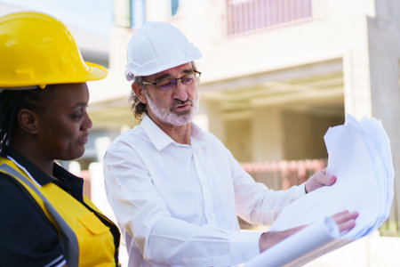 Team of engineer discuss at construction site. Female black ethnicity engineer taking to caucasian white client about the construction plan in blue print.の写真素材