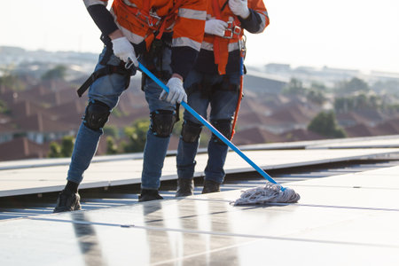 Professional electrical engineers working on the residential rooftop to clean up the dusty solar panels.の写真素材