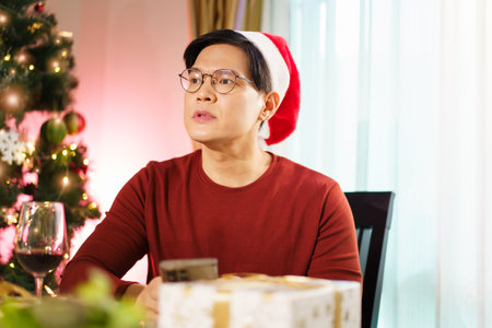 Asian lonely man is sitting alone at dining table in Christmas night, a man waiting for someone coming. Unhappy man feels drunk.の写真素材