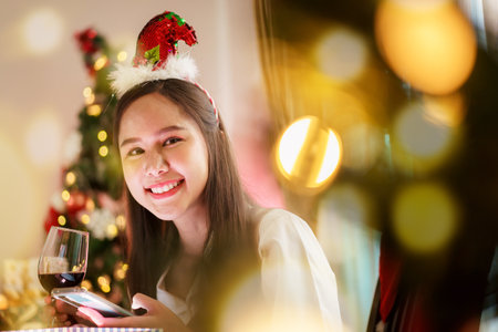 A beautiful Asian woman is excited to open Christmas presents during her Christmas dinner in a cozy and warm living room at home. She is enjoying celebrating Christmas night alone.の写真素材