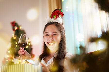 A beautiful Asian woman is excited to open Christmas presents during her Christmas dinner in a cozy and warm living room at home. She is enjoying celebrating Christmas night alone.の写真素材
