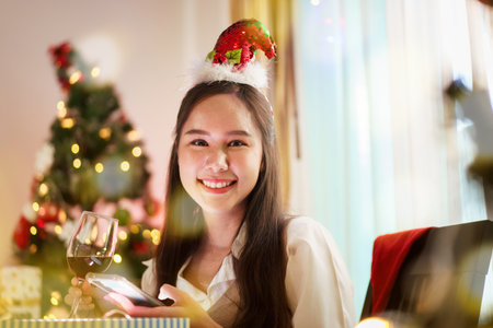 A beautiful Asian woman is excited to open Christmas presents during her Christmas dinner in a cozy and warm living room at home. She is enjoying celebrating Christmas night alone.の写真素材