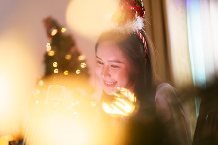 A beautiful Asian woman is excited to open Christmas presents during her Christmas dinner in a cozy and warm living room at home. She is enjoying celebrating Christmas night alone.の写真素材