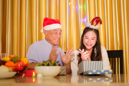 Asian happy family with father and daughter are celebrating the Christmas party together in cozy and warm living room at home. An elderly Asian man is giving his daughter the Christmas present.の写真素材