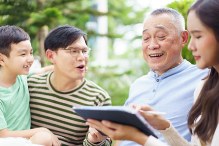 Happy Asian family are sitting in backyard garden at home and talking together. A multi generation Asian family people. Man and woman with a little child talking to grandfather.の写真素材
