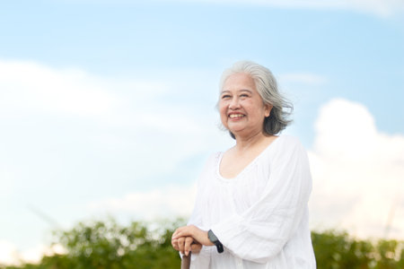 Happy cheerful Asian elderly woman is enjoying an outdoor activity in the daytime. Happy and healthy Asian woman is walking outside for daily exercise. Health care, wellness, and wellbeing concept.の写真素材