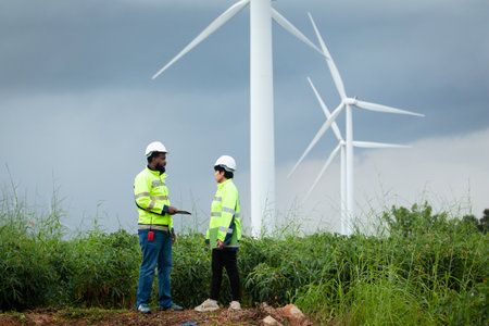 Team of electricians engineer are having a conversation and discussion together at electric generator windmill station. Female and male professional engineers are working at electric wind turbine.の写真素材